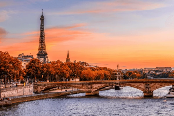 Paris in the fall, with bright orange and red trees lining the river and the Eiffel Tower rising up in the background