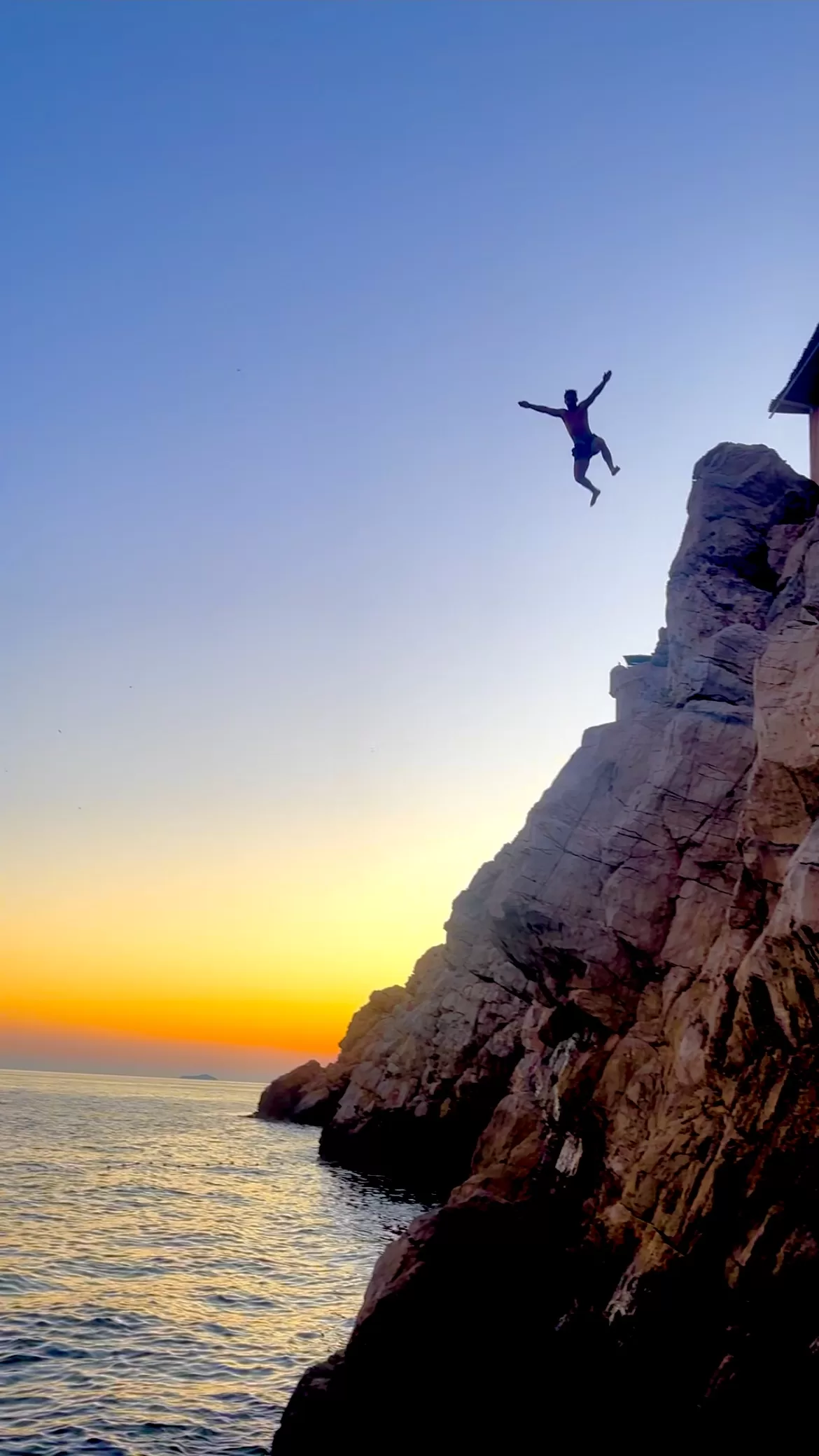 me cliff jumping at the buža beach bar in dubrovnik, with the sunset in the background.