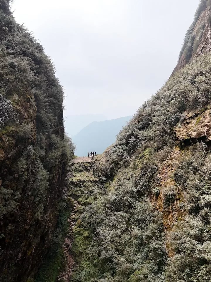 drone shot of group of people standing on a narrow ledge between two mountains faces