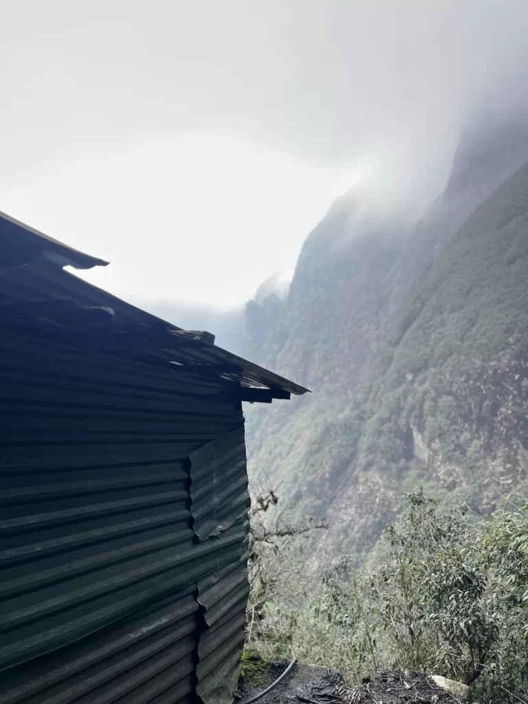green structure on a mountainside overlooking mountains in the clouds