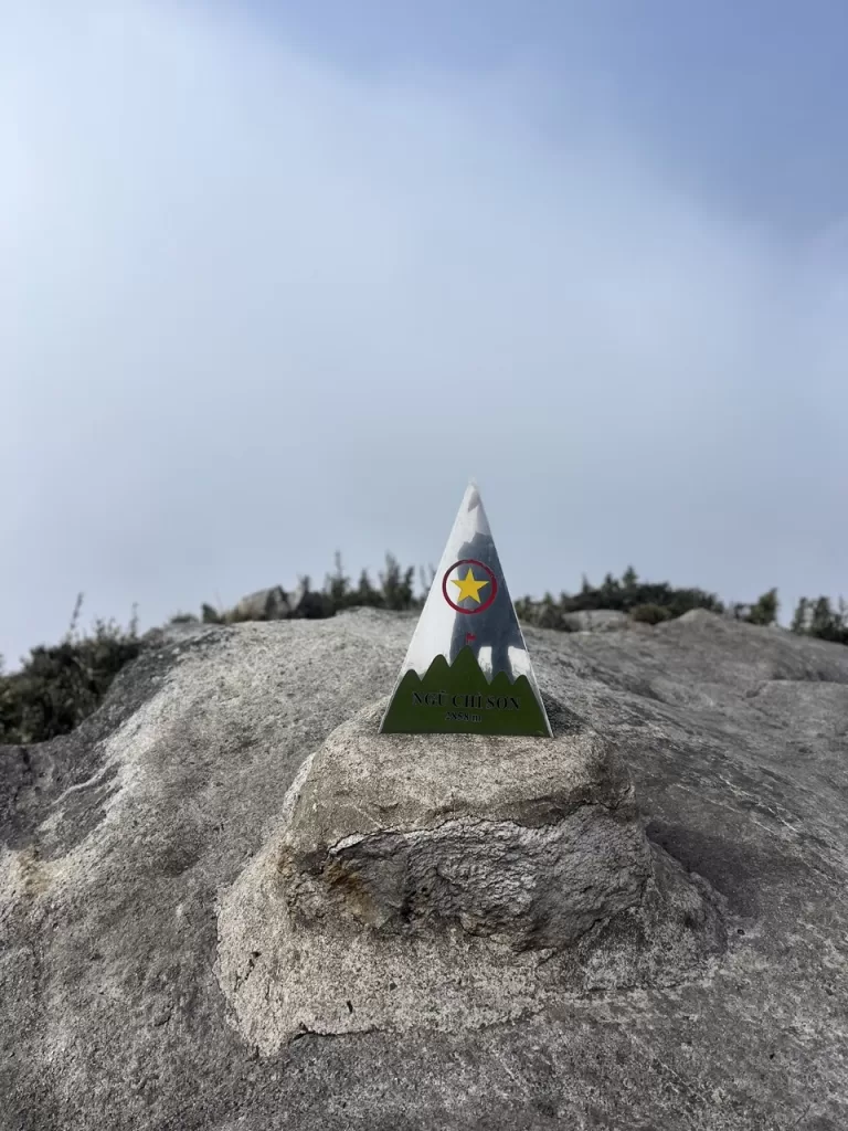 steel pyramid-shaped summit marker on a plinth at the top of a mountain with clouds in the background