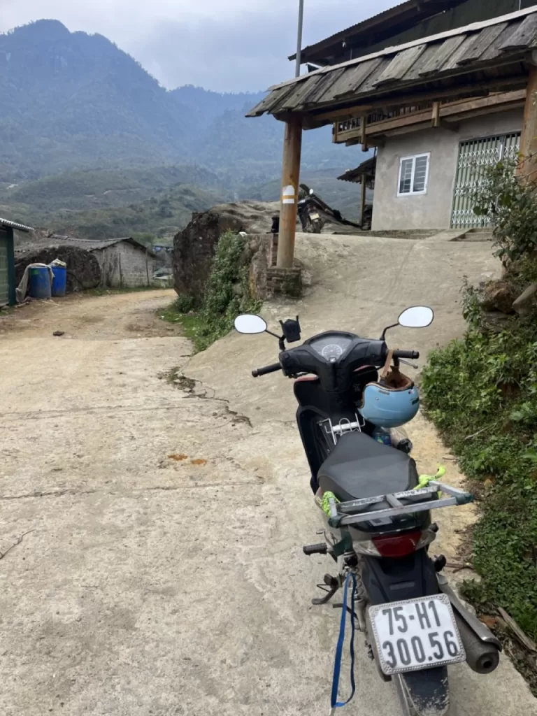 motorbike parked on the road next to homestay with mountains in the background