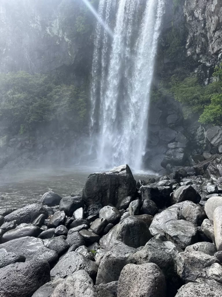 a collection of stones in front of a strong waterfall falling fast into a small pool with mist rising around the area