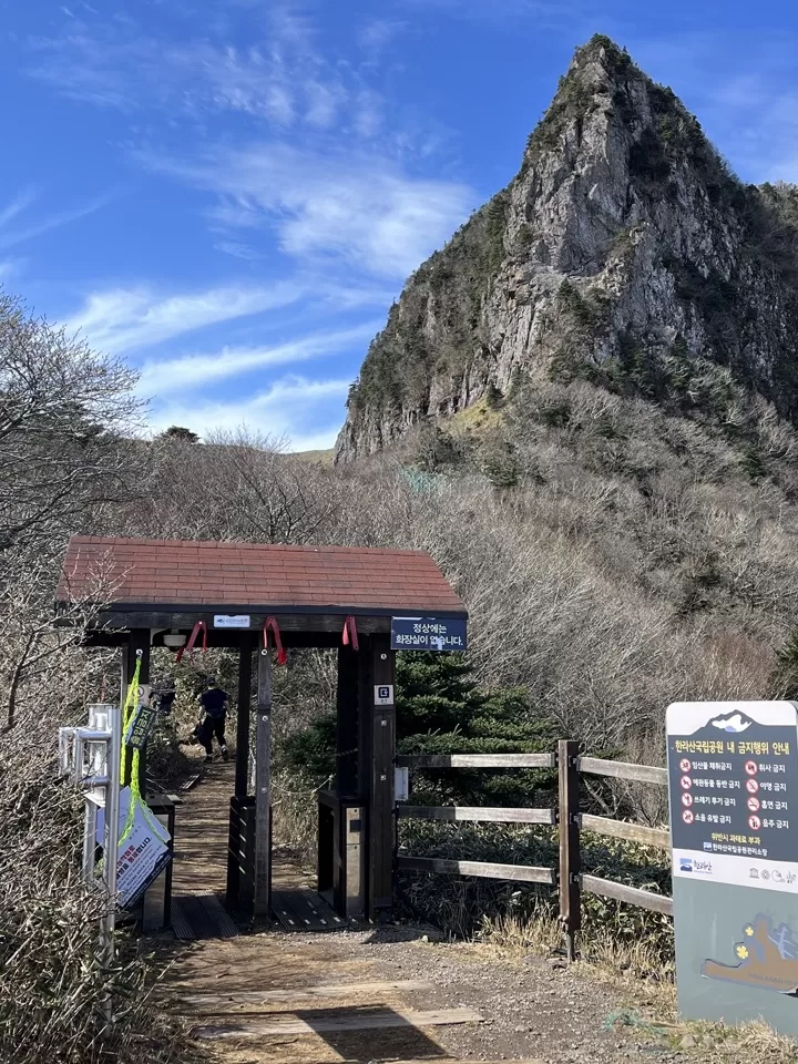 mountain trail with a turnstile gate in front of a sharp mountain peak under a clear blue sky