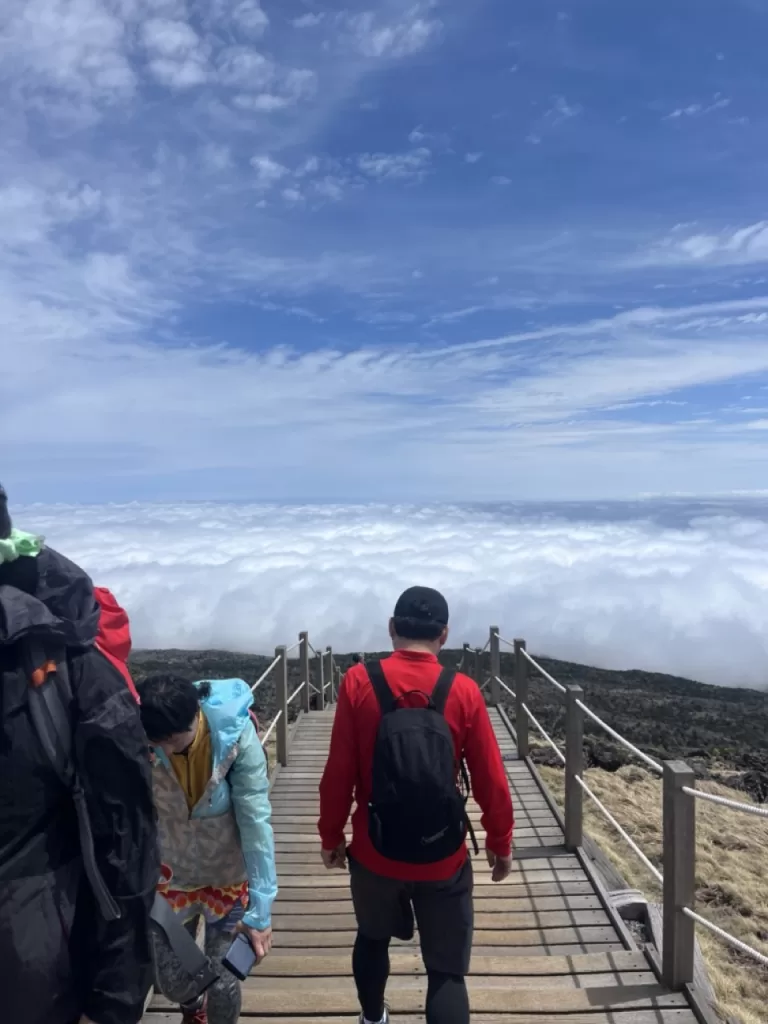 man walking down trail overlooking sea of clouds rolling underneath