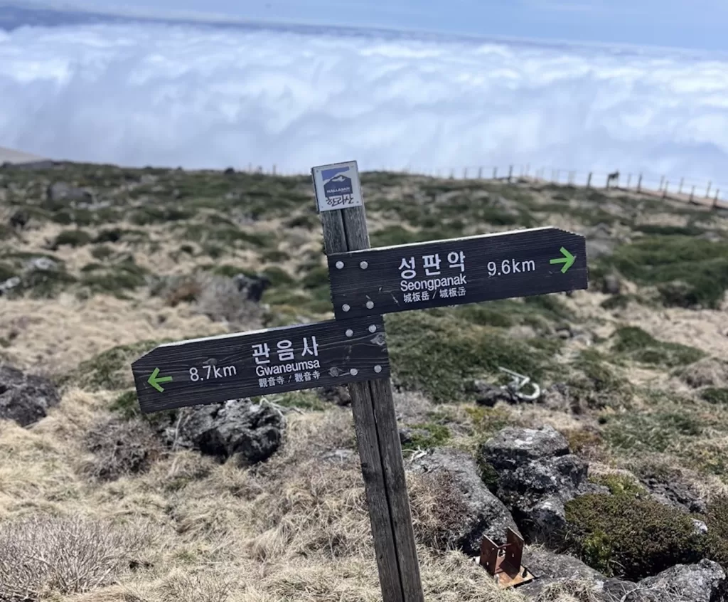 trail marker high on a mountain on dry looking terrain with a sea of clouds rolling underneath