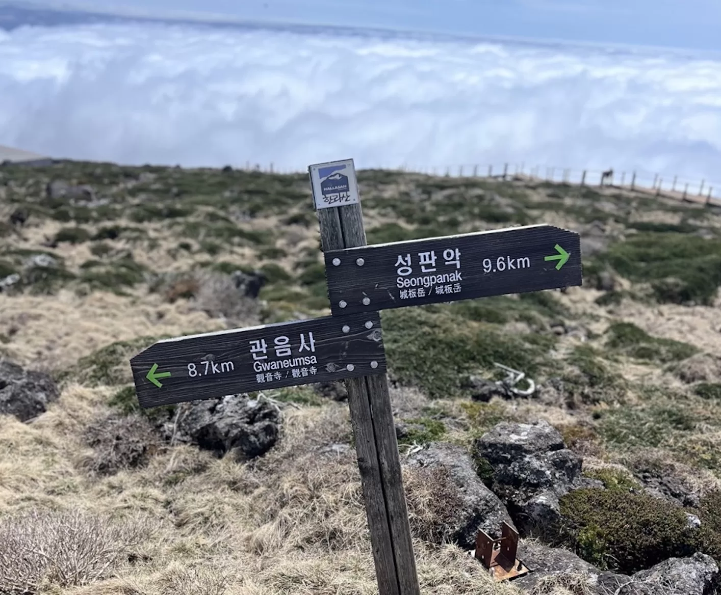 trail marker high on a mountain on dry looking terrain with a sea of clouds rolling underneath