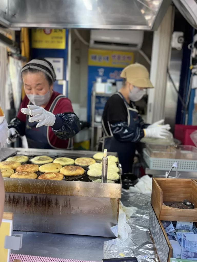 two korean ladies frying hotteoks, a korean street food snack
